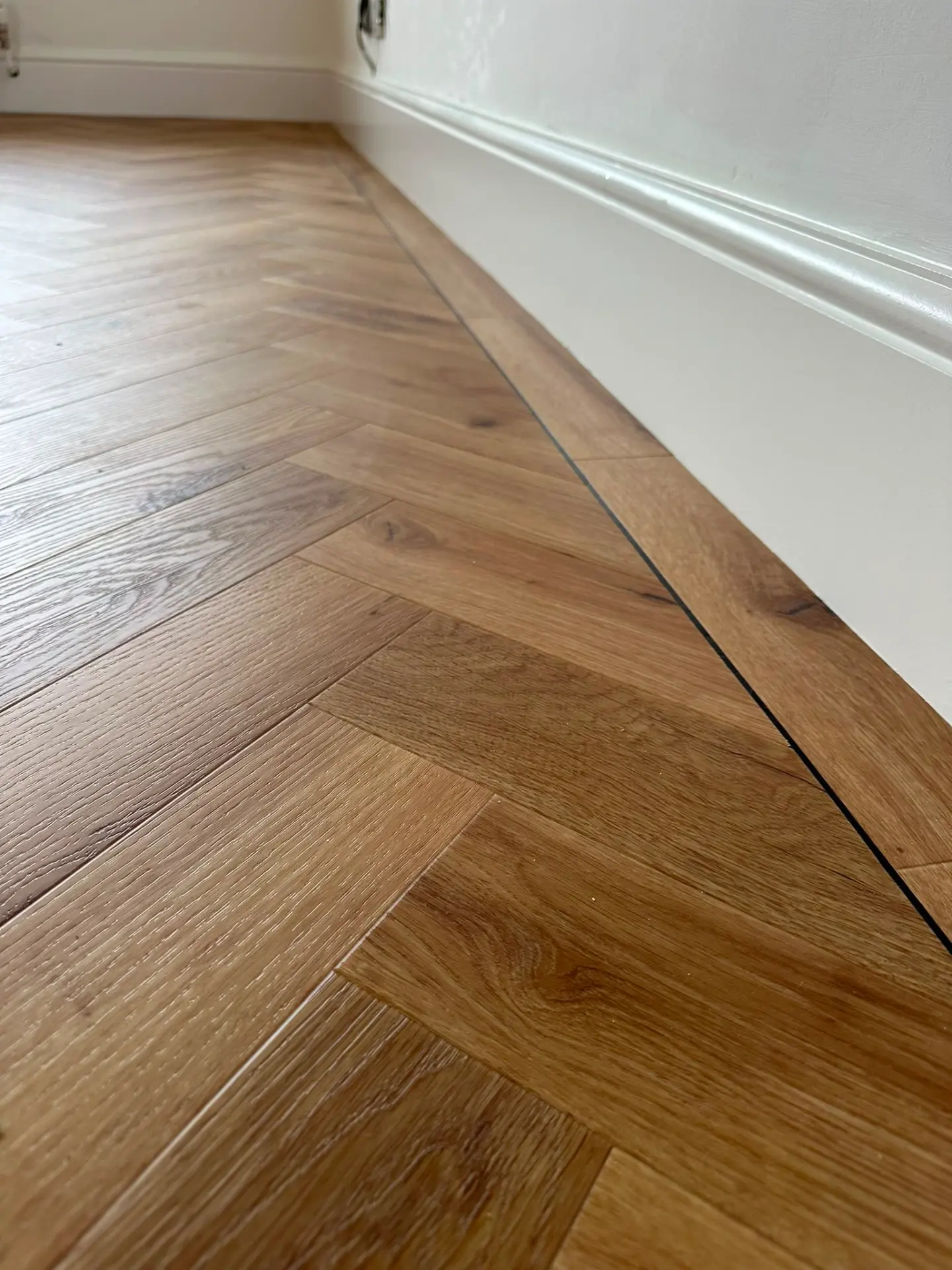 Close-up of herringbone LVT flooring with a black feature strip along the skirting